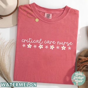 Puede incluir: Camiseta de color sand&iacute;a con el texto "critical care nurse" en letras blancas y una fila de margaritas blancas debajo del texto.
