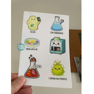 May include: A sheet of stickers featuring science-themed illustrations. Designs include a cell taking a selfie, a beaker with coffee, a petri dish with smiling cells, a lab machine, a beaker with a "This is fine" meme, and a germ with the text "I grow on people."