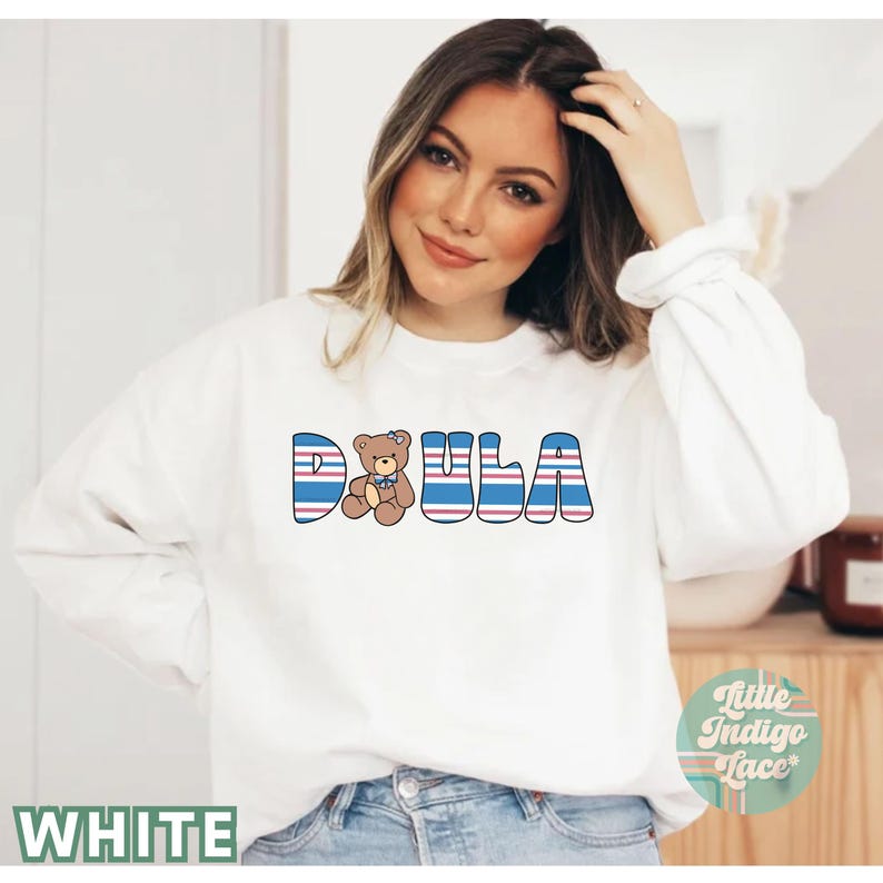 May include: White sweatshirt with blue and red stripes spelling out "DOULA" with a brown teddy bear wearing a blue bow in the middle of the word.