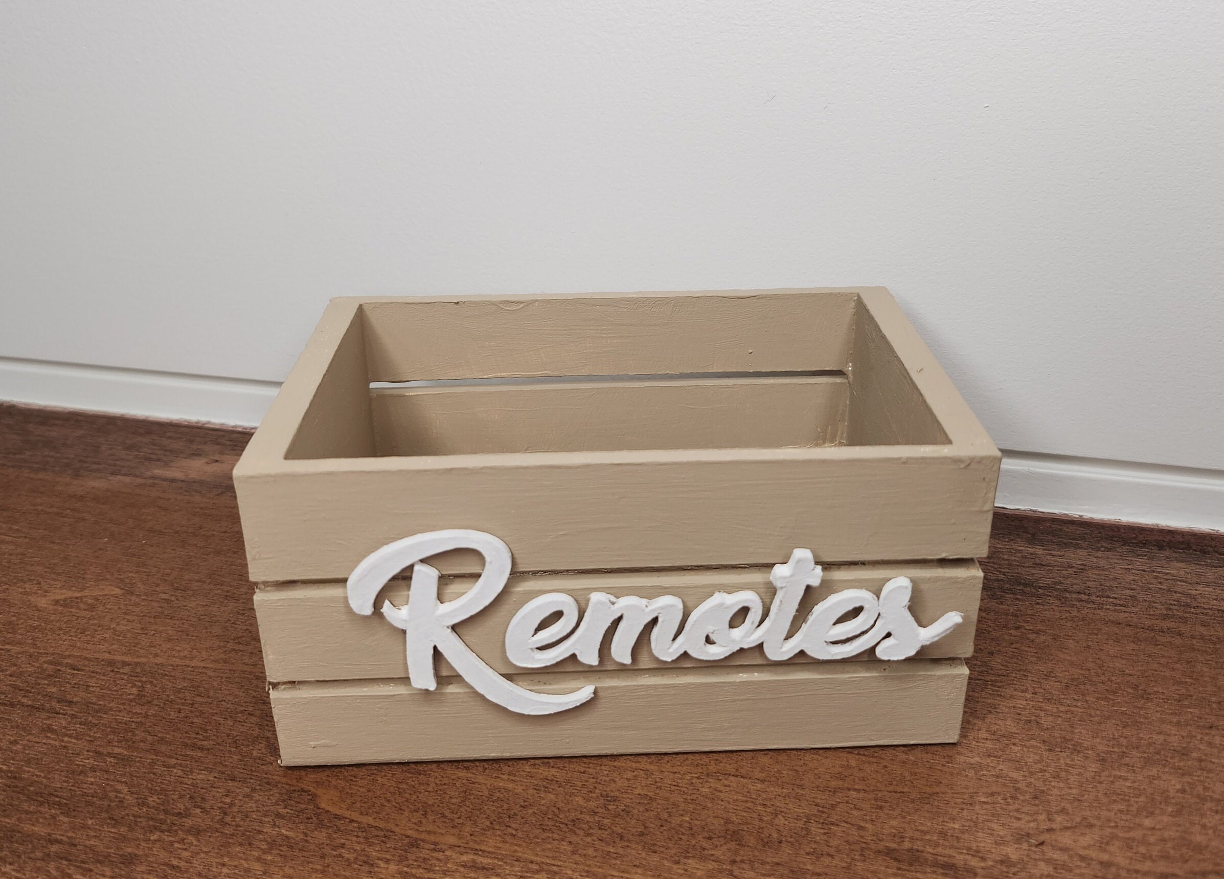 Beige wooden mini crate with a white Remotes word. The crate is perfect for farmhouse or modern decor. Ideal for remote controls organization and decorative accents.