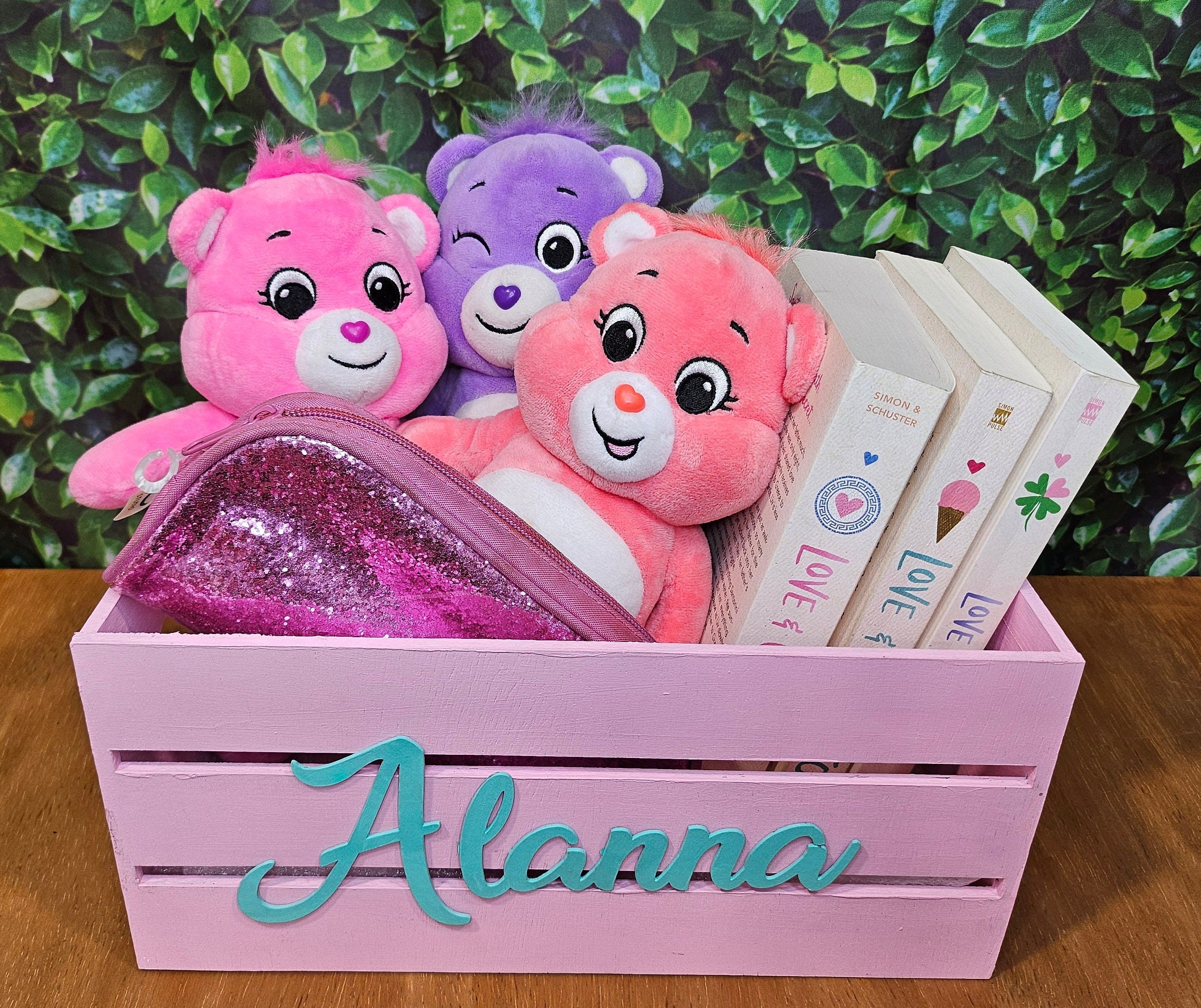 A pink wooden crate with teal name . Ideal for organizing books or adding a decorative touch to a nursery or kids room.