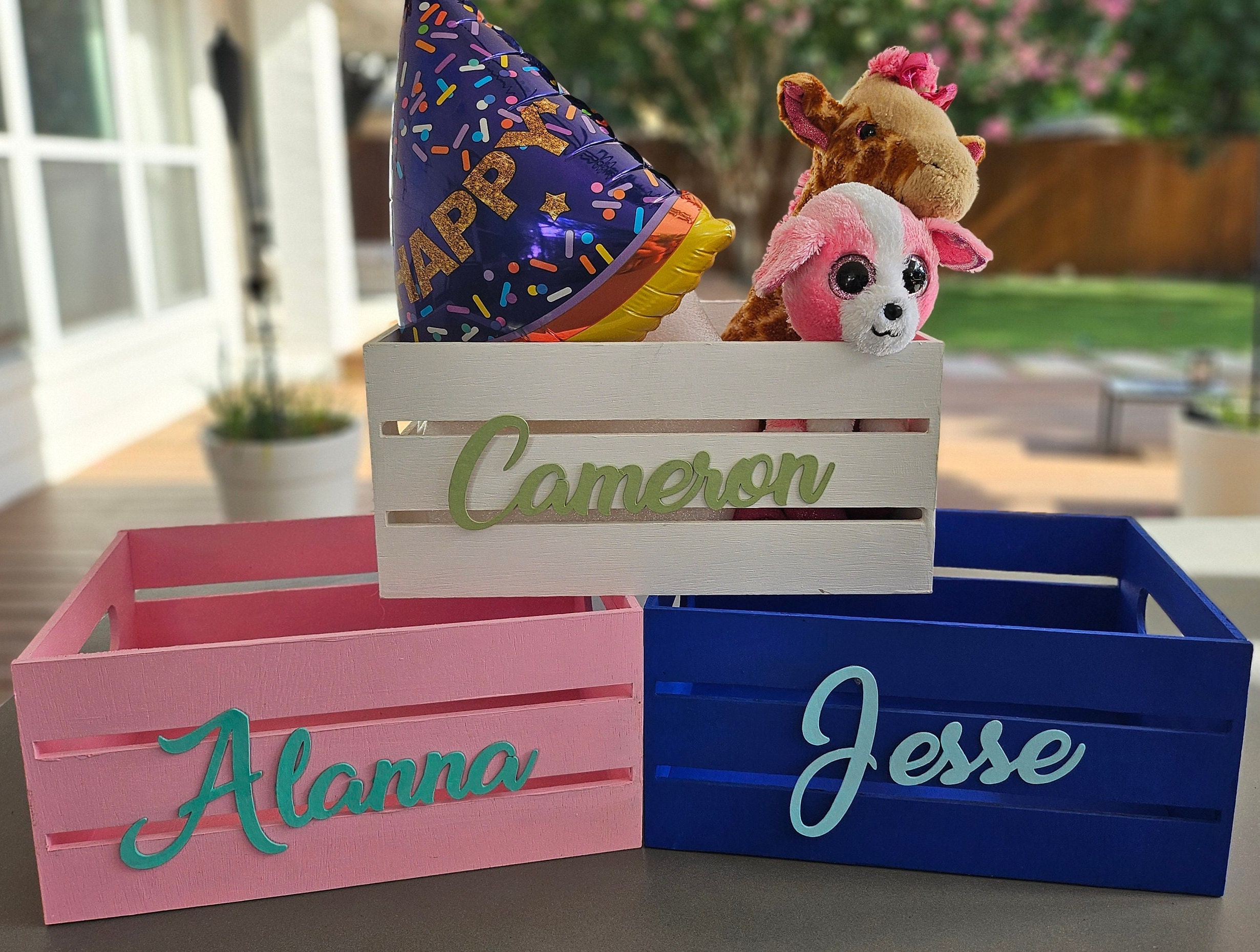 Three personalized wooden boxes. Names are hand-painted in different colors: green, sage, teal, and light blue. The boxes are white, pink, and blue. Ideal for a personalized gift or adding a decorative touch to a nursery or kids room.