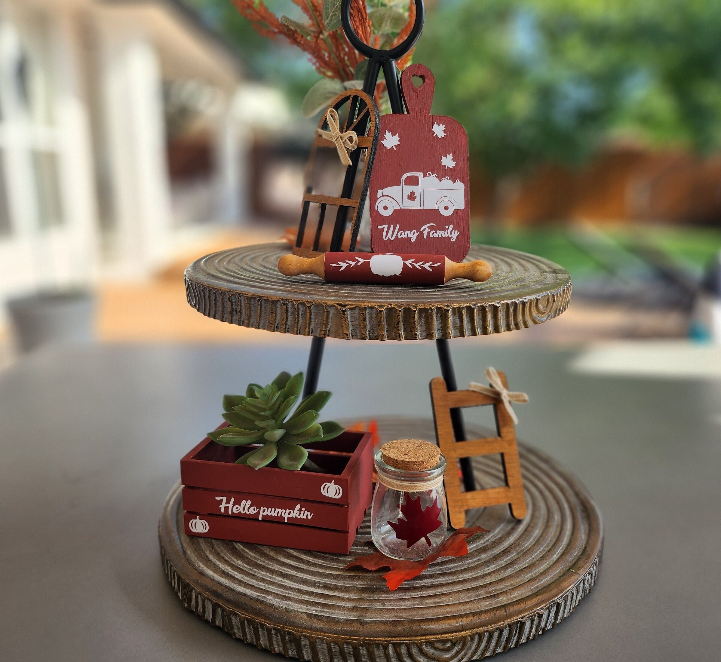 Two-tiered wooden stand with fall decor including a red rust mini crate with custom vinyl inscription, a jar with a maple leaf, a red cutting board with white custom vinyl design, red rust rolling pin, stained mini window and small rustic ladder.