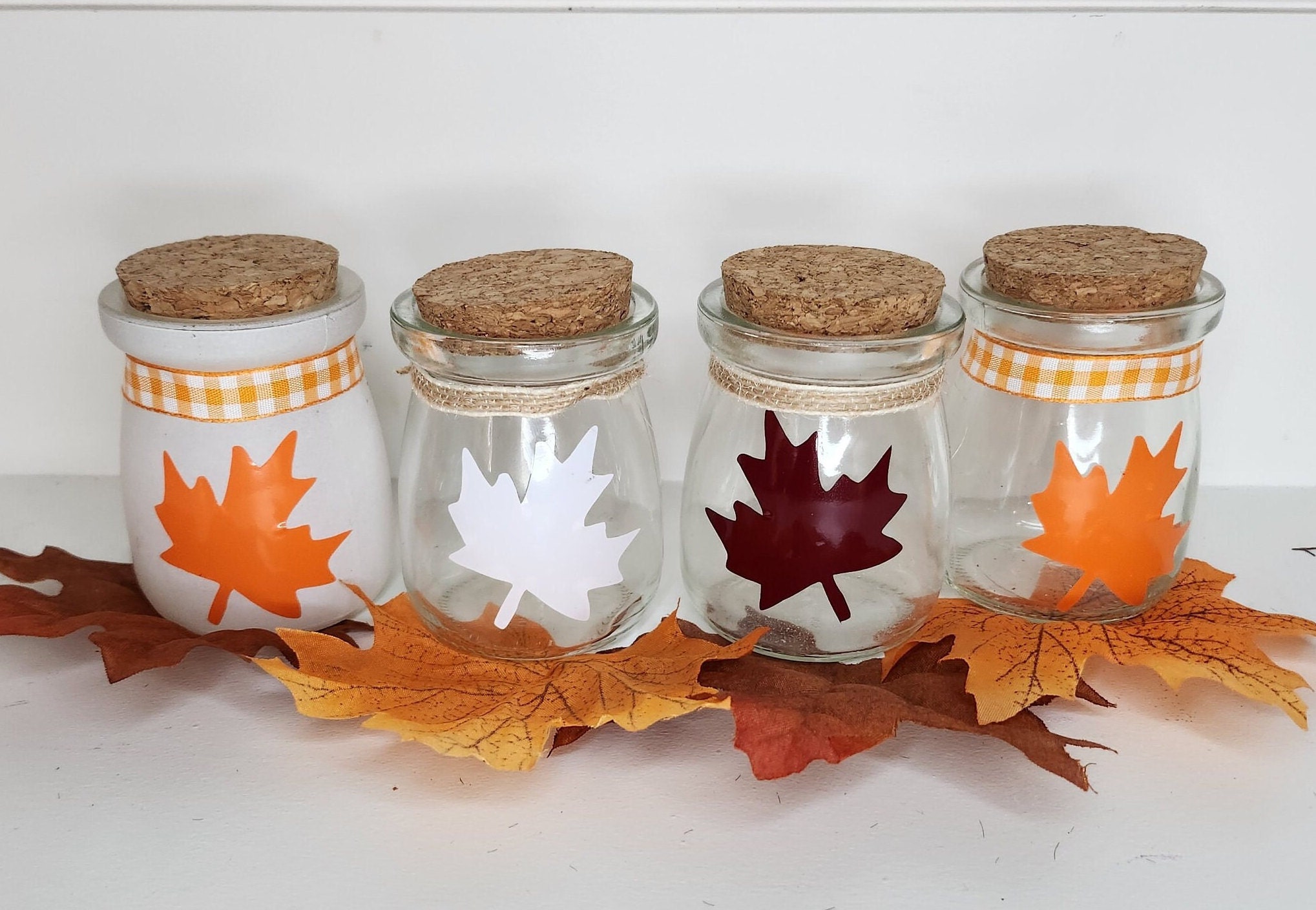 Four mini glass jars with maple leaves for fall decor.