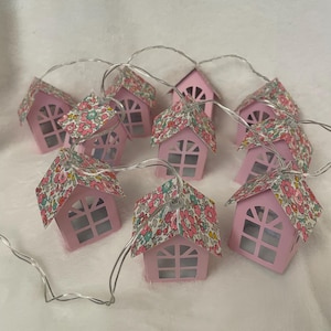 May include: A string of pink paper house lights with floral patterned roofs. The lights are strung together with a silver wire.