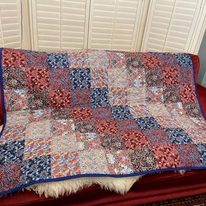 May include: A patchwork quilt with a blue, red and white floral pattern. The quilt is folded and placed on a red sofa.
