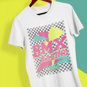 May include: White t-shirt with a checkered pattern and geometric shapes in pink, yellow, and green. The text "BMX RACING 1969" is printed in a retro font.