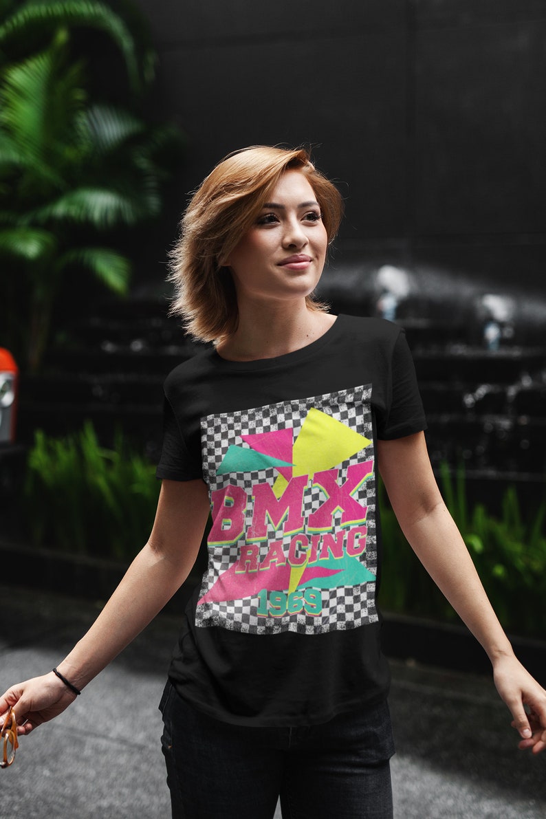 May include: Black t-shirt with a retro-style graphic design featuring a checkered background, pink, yellow, and green geometric shapes, and the text "BMX RACING 1989".