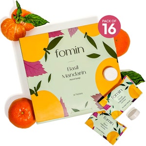 May include: A box of 16 hand soap tablets in a green and yellow box with a mandarin orange design. The box says "fomin Basil Mandarin Hand Soap 16 Tablets". There are two individual tablets wrapped in clear plastic with a green and yellow design. The text on the individual tablets says "fomin Basil Mandarin Hand Soap".