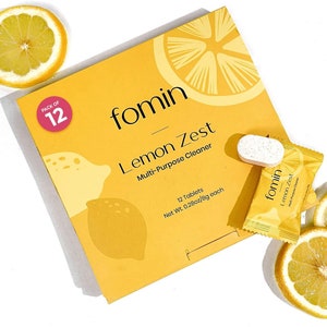 May include: A yellow box with a lemon design and the text "fomin Lemon Zest Multi-Purpose Cleaner" on it. The box contains 12 tablets, each weighing 0.28 ounces or 8 grams. A single tablet is shown next to the box, along with a small yellow packet containing a tablet.