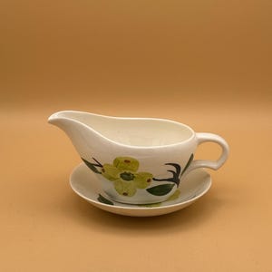 May include: White ceramic gravy boat with a matching saucer. The set features a floral design with yellow and green accents. The gravy boat has a spout and a handle. The saucer is round and complements the boat's design.