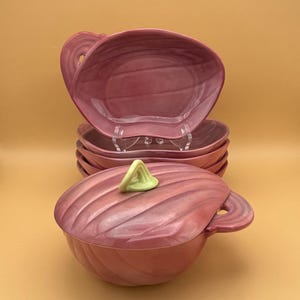 May include: A set of six pink ceramic bowls with a swirl design. The bowls have a green knob on the lid and a handle on the side.