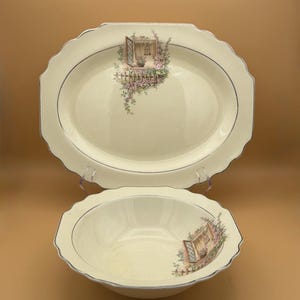 May include: Cream-colored oval serving platter and bowl set. Each piece features a decorative illustration of a window with floral accents. The set has a scalloped edge and a thin blue trim.