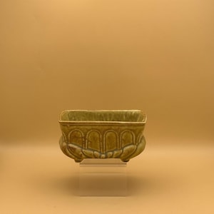 May include: A small, rectangular, green ceramic planter with a decorative design and three feet.