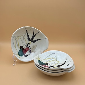 May include: Set of four white ceramic bowls with a textured surface and a black and white bird design. The bowls have a green, red, and black floral pattern.