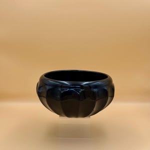 May include: A glossy black ceramic bowl with a rounded, scalloped exterior design featuring vertical ridges that create a petal-like appearance. The bowl has a wide, open circular rim and a smooth, reflective surface finish throughout the piece.