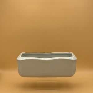 May include: A white ceramic rectangular planter with a slightly scalloped rim. The planter is sitting on a clear acrylic stand.