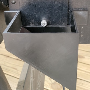 May include: A black metal grill with a black metal drip tray attached to the bottom. The drip tray is angled to direct grease away from the grill.
