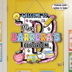 May include: A decorative classroom door sign shaped like a large letter B with a lined paper background. It features the text "WELCOME TO Mrs. BARRERA'S CLASSROOM" and "LET'S LEARN TODAY" with illustrations of a lightbulb, pencil, school bus, and books.
