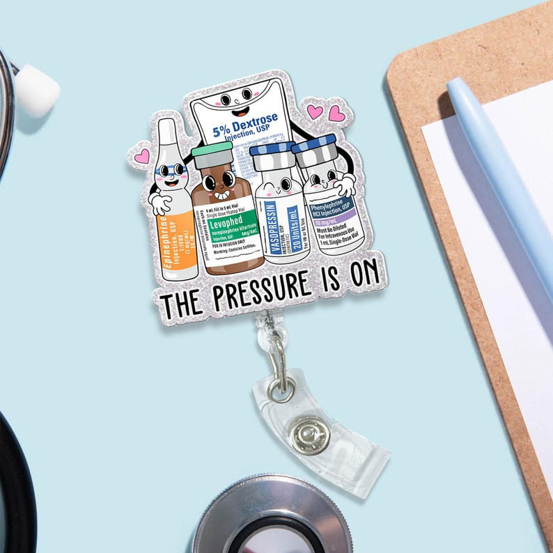 May include: A clear badge reel with a cartoon design featuring medicine vials and the text "THE PRESSURE IS ON." The vials include "Epinephrine," "Levophed," "Vasopressin," and "5% Dextrose." The badge reel has a clear plastic strap and a metal clip.