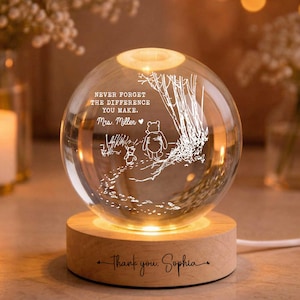 May include: A clear glass globe with an etched Winnie the Pooh scene, resting on a wooden base. The globe has the text "NEVER FORGET THE DIFFERENCE YOU MAKE. Mrs. Miller" and "thank you Sophia". The base is illuminated with a warm glow.