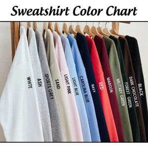 May include: Color chart showing 12 different sweatshirt colors, including white, ash, sports grey, sand, light pink, light blue, carolina blue, navy, red, maroon, military green, dark chocolate, and black.