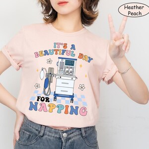 May include: A pink t-shirt with a colorful graphic of a medical ventilator and the text "It's a beautiful day for napping".