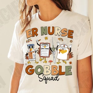 May include: White t-shirt with a Thanksgiving theme. The text "ER Nurse Gobble Squad" is printed in brown, green, and orange. The design includes a turkey, a vial of medication, and an AMA form.