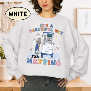 May include: White sweatshirt with a graphic of a medical ventilator and the text "It's a beautiful day for napping" in colorful letters.