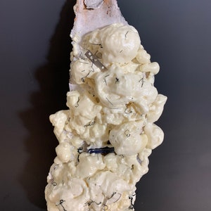 May include: A white foam sculpture with black wire and metal pieces embedded in it. The sculpture is on a gray background.