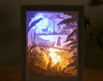 Könnte beinhalten: Eine weiße Papierlampe mit einem 3D-Design einer Waldszene. Die Szene zeigt ein Reh, ein Mädchen und Kaninchen. Die Lampe wird mit einem warmweißen Licht beleuchtet.