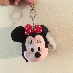 Pu&ograve; includere: Portachiavi in ​​peluche di Minnie Mouse con fiocco rosso a pois e orecchie nere. Il portachiavi ha una catena e un fermaglio in metallo argentato. &Egrave; attaccata un'etichetta Disneyland.