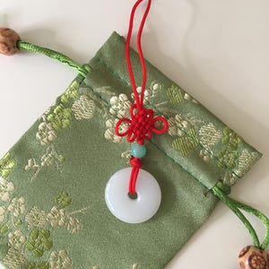 May include: A white jade pendant with a red string and a knot, hanging from a green drawstring bag with floral pattern.