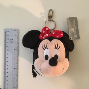 Pu&ograve; includere: Portachiavi di Minnie Mouse in peluche con fiocco rosso a pois. Il portachiavi ha una chiusura argentata e un'etichetta con la scritta "Hong Kong Disneyland". La testa di Minnie Mouse &egrave; nera, bianca e rosa.