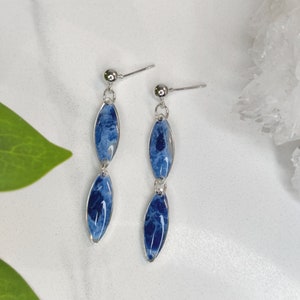 May include: A pair of silver dangle earrings with two blue and white oval-shaped resin pieces on each earring.