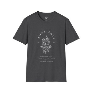 May include: A dark heather grey t-shirt with a white graphic print of a floral design and the text "AMOR FATI = "LOVE YOUR FATE" WHICH IS IN FACT YOUR LIFE -FRIEDRICH NIETZSCHE"