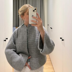 May include: A grey crocheted cardigan with long sleeves and a slightly cropped fit.