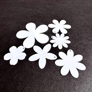 May include: White flower-shaped cutouts in various sizes, each with a small hole for hanging. The cutouts are arranged on a dark gray surface. These craft supplies are ideal for DIY projects.