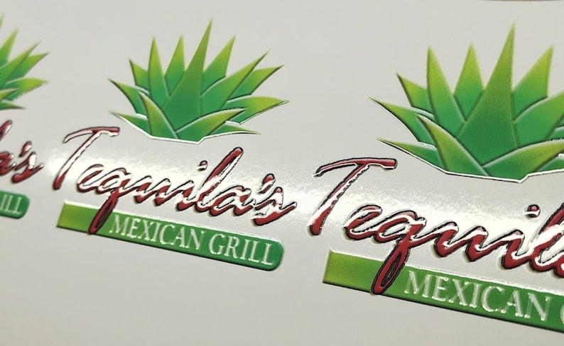 May include: A close-up of a silver and white sticker with a green agave plant and the text "Tequila's Tequila" in red lettering. The text "Mexican Grill" is also included in green lettering.