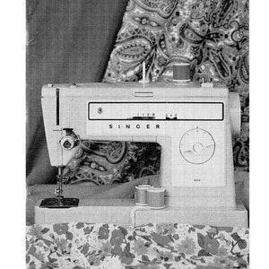Op de afbeelding: Een zwart-witfoto van een Singer 522 naaimachine. De machine is wit en heeft een zwart Singer-logo op de voorkant. De machine staat op een stof met een patroon.