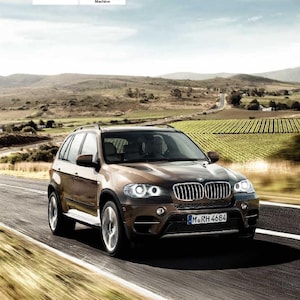 Könnte beinhalten: Ein brauner BMW X5 fährt auf einer asphaltierten Straße mit grünen Hügeln und Weinbergen im Hintergrund. Das Auto hat ein Nummernschild mit der Aufschrift "M RH 4684". Der Text "Contents A-Z" und "Online Edition for Part no. 01 40 2 606 735-03-11 500" ist ebenfalls sichtbar.