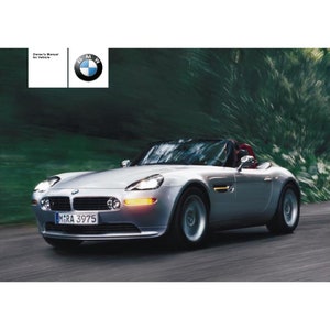 Puede incluir: Un BMW Z8 roadster plateado conduciendo por un camino sinuoso con árboles verdes en el fondo. El coche tiene una matrícula negra que dice "M1RA 3975".