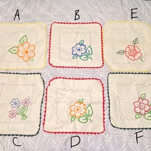 May include: Six white embroidered tea towels with different floral designs. Each towel has a crocheted border in a different color: yellow, red, green, black, yellow, and black.