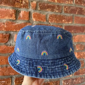 Könnte beinhalten: Ein blauer Jeans-Bucket-Hut mit gestickten Regenbogen-Designs.