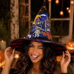 May include: A pointed witch hat featuring a vibrant graphic print of a haunted house, a mummy, and orange jack-o'-lanterns against a dark blue night sky. The underside of the wide brim displays a pattern of alternating black and red horizontal stripes.