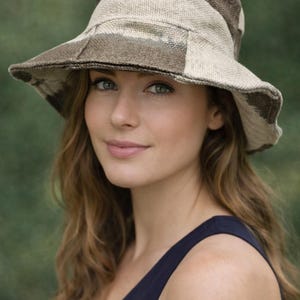 May include: A beige and brown patterned sun hat with a wide brim. The hat has a patchwork design and is made of a textured fabric. The hat is worn by a person wearing a navy blue tank top.