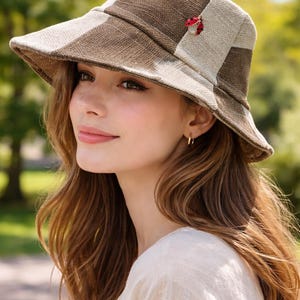 May include: A brown and beige bucket hat with a wide brim. The hat features a ladybug pin on the side. The hat is made of a woven material and has a classic, casual style.