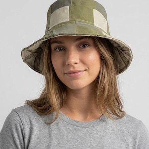 May include: A patchwork bucket hat in shades of green and beige. The hat features a wide brim and a geometric pattern, offering a stylish and practical accessory. The hat is made of a durable fabric.