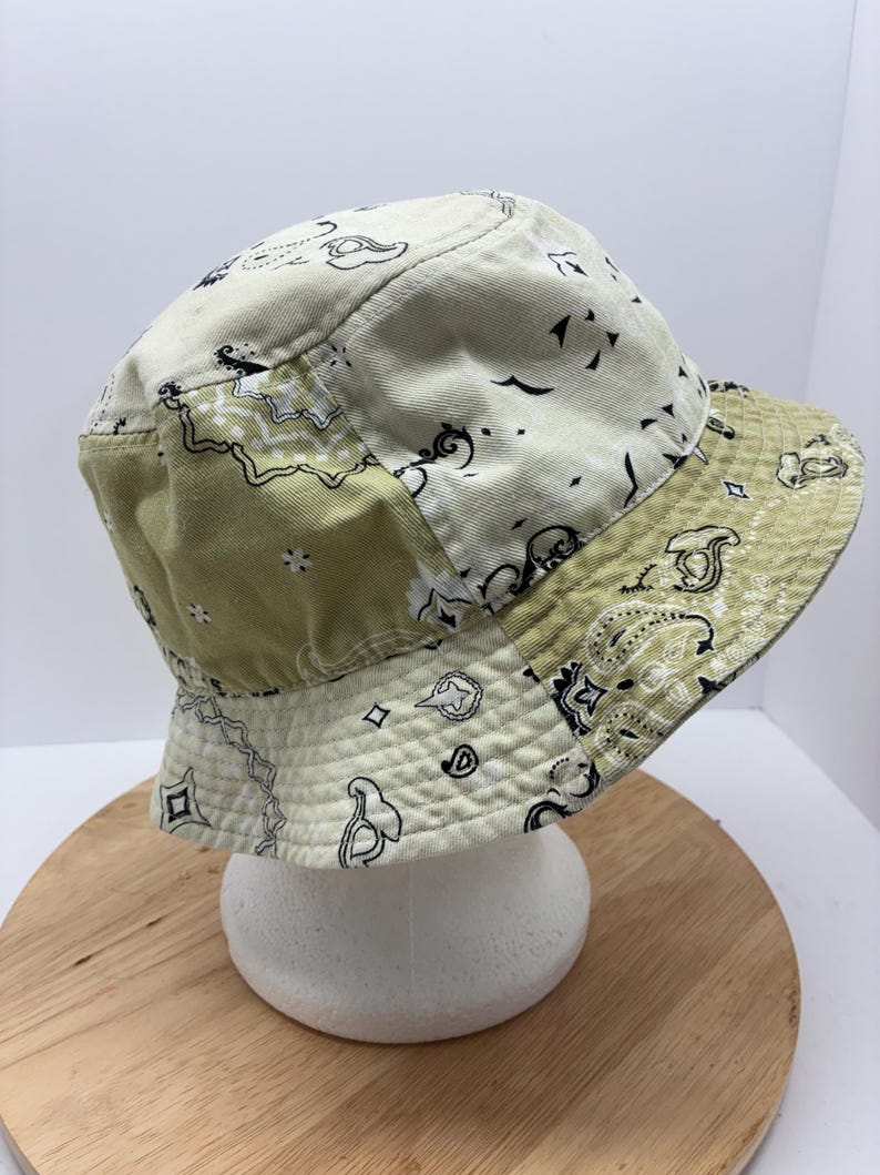 May include: A patchwork bucket hat in shades of cream and olive green. The hat features a paisley pattern in black and white. The hat is made of a soft, possibly cotton, material.