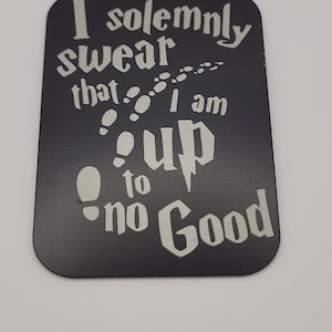 May include: Black metal sign with white text that reads "I solemnly swear that I am up to no good." The text is surrounded by a series of white footprints.